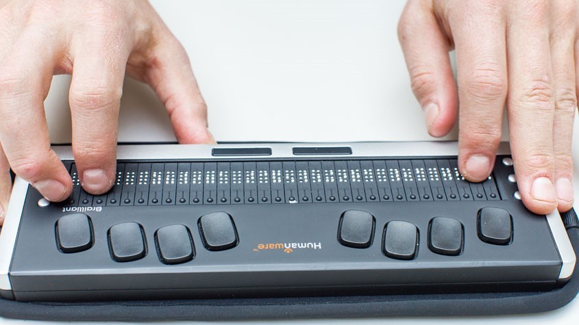 Two hands typing on an electronic braille display